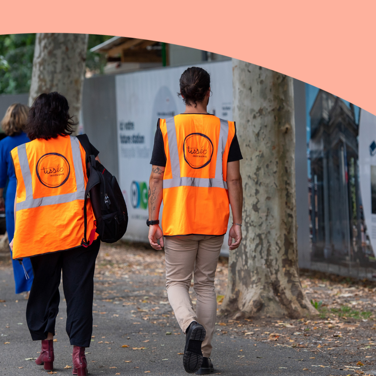 Deux personnes de dos avec un gilet orange avec un logo Tisséo Ingenierie qui marchent près du chantier de la ligne C de Toulouse